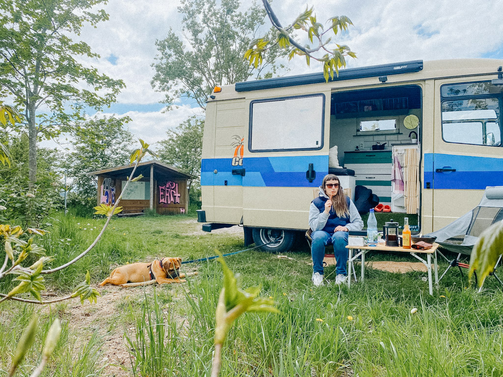 Lisa Ludwig steht mit Hund Frau Maier und ihrem Freund an den Plothener Teichen in Thüringen mit dem selbstausgebauten Campervan