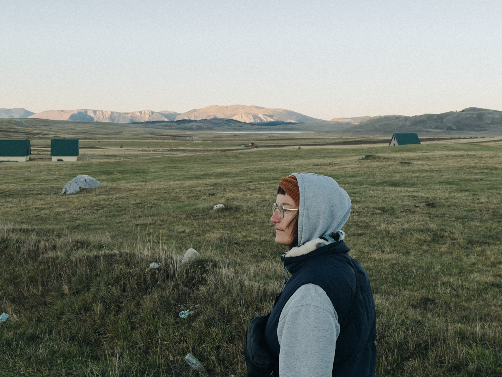 Lisa Ludwig steht am Durmitor Nationalpark mit herbstlicher Kleidung, blickend auf den Sonnenuntergang